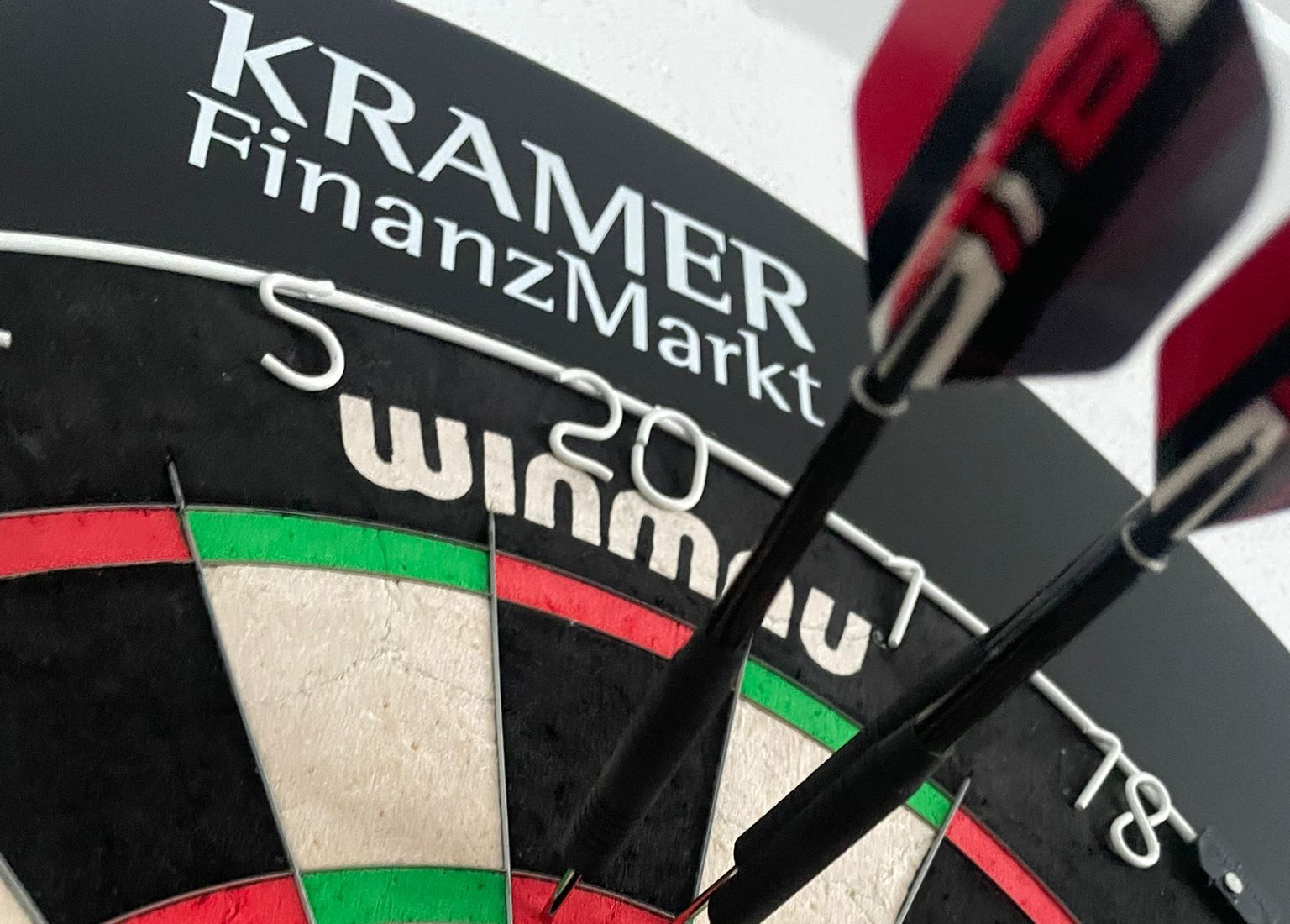 Dartscheibe mit dem Schriftzug KRAMER FinanzMarkt, zwei Pfeile stecken in der Triple 20